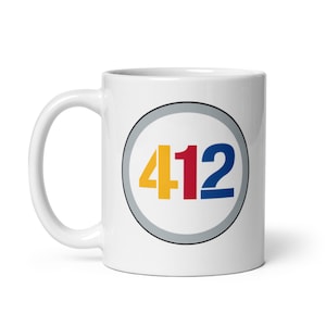 May include: White ceramic mug with a gray circle containing the number 412 in yellow, red, and blue.