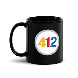 May include: Black ceramic coffee mug with a white circle containing the number 412 in yellow, red, and blue.