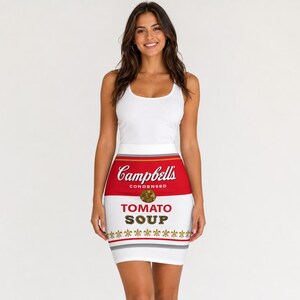 Op de afbeelding: Witte minirok met een Campbell's Tomato Soup-blikontwerp. De rok heeft een rode bovenband met het Campbell's-logo, een wit middengedeelte met de tekst "TOMATO SOUP" en een grijze en gouden onderrand.