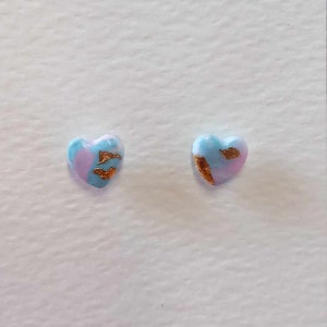May include: A pair of heart-shaped earrings with a blue and pink marbled design and gold accents. The earrings are displayed on a white card.