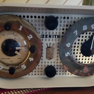 May include: A white Zenith radio with two round dials. The left dial has a clock face with black hands and the numbers 1-12. The right dial has the numbers 5-16. The radio has a white and black grid pattern.