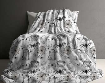 May include: White Halloween-themed blanket with a repeating pattern of black line art. The design includes ghosts, bats, spiderwebs, cauldrons, and tombstones with "R.I.P." text. The blanket is draped over a pillow.