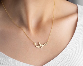 May include: A gold necklace with a delicate chain and a pendant featuring the Arabic word "Sumaya" in a cursive script.