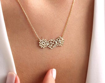 May include: A gold necklace with a delicate chain and a pendant featuring three cutout flowers. The flowers are a rose, a daisy, and a smaller flower with five petals.
