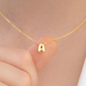 May include: A gold chain necklace with a small, puffed letter 'A' pendant.