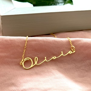 Può includere: Collana d'oro con il nome "Olivia" scritto in corsivo.