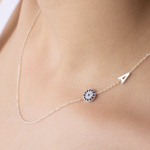 May include: A silver necklace featuring a blue evil eye charm and a letter 'A' pendant.