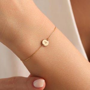 May include: A delicate gold chain bracelet with a small round charm featuring the letter 'A'.