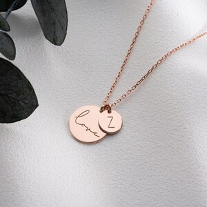 May include: A rose gold necklace with two charms. One charm is a circle with the word "love" written in cursive. The other charm is a circle with the letter "Z" engraved on it.