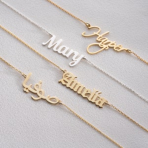 May include: Four gold necklaces with different names on them. The names are "Harper", "Amelia", "Mary", and an Arabic name. The necklaces are on a white background.