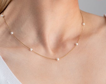 Peut inclure: Un collier délicat en chaîne dorée avec cinq petites perles blanches espacées uniformément le long de la chaîne.