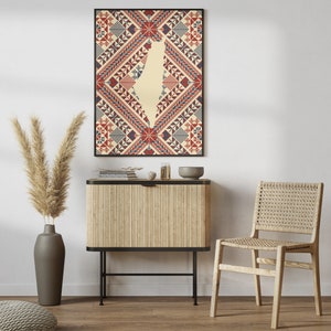 May include: A framed print of a geometric pattern in red, blue, and white with the outline of the country of Israel in the center. The print is hanging on a white wall above a wooden cabinet with a black metal frame. A woven chair is in the foreground.