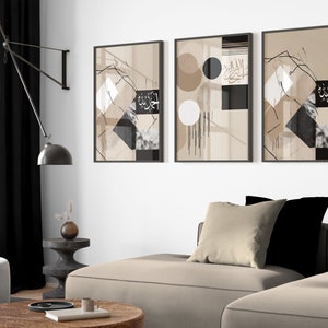 Puede incluir: Tres impresiones de arte abstracto enmarcadas con formas geométricas y caligrafía árabe en tonos negro, blanco y beige. Las impresiones están colgadas en una pared blanca sobre un sofá beige.