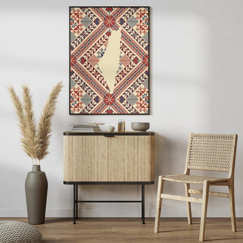 May include: A framed print of a geometric pattern in red, blue, and white with the outline of the country of Israel in the center. The print is hanging on a white wall above a wooden cabinet with a black metal frame. A woven chair is in the foreground.