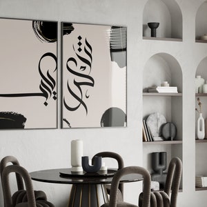 Peut inclure: Deux impressions d'art encadrées avec une calligraphie noire abstraite sur fond beige. L'œuvre présente des coups de pinceau et des formes noirs. Les impressions sont exposées dans une salle à manger moderne avec une table ronde et des chaises.