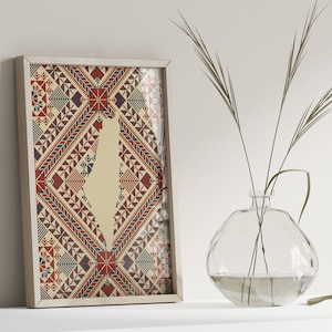 May include: A framed print of a stylized map of Israel with a red, white, and blue geometric pattern. The print is hanging on a white wall with a vase of dried grass in the foreground.