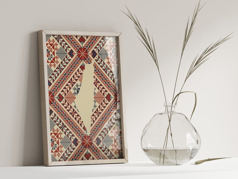 May include: A framed print of a stylized map of Israel with a red, white, and blue geometric pattern. The print is hanging on a white wall with a vase of dried grass in the foreground.