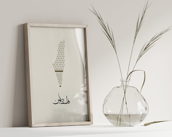 May include: Framed art print featuring a minimalist illustration of Palestine's map in shades of beige and olive green. The Arabic word for Palestine is written in black script below the map. A clear glass vase with dried plants is next to the framed art.