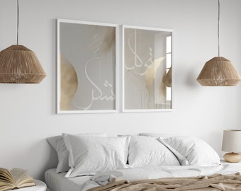 May include: Two framed abstract art prints with white calligraphy on a light gray background with gold accents. The prints are hanging on a white wall above a bed with white bedding and brown throw pillows.