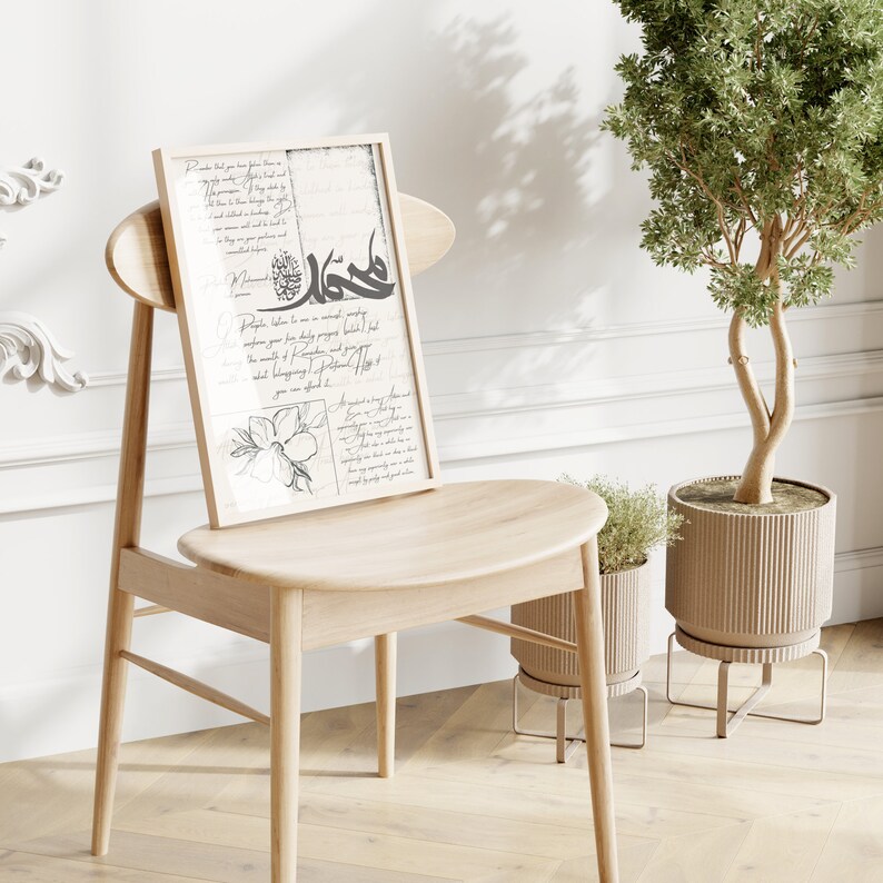 May include: A framed print with a black and white design of Arabic calligraphy and a floral illustration. The print is hanging on a wall behind a wooden chair. There are two potted plants in the foreground.