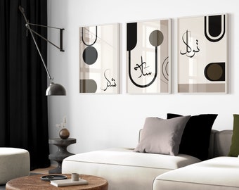 Puede incluir: Tres impresiones artísticas enmarcadas con formas geométricas en tonos beige, negro y marrón. Cada impresión presenta caligrafía árabe. La obra de arte cuelga sobre un sofá blanco con cojines decorativos, creando una estética moderna.