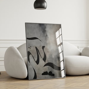 Könnte beinhalten: Ein gerahmter abstrakter Kunstdruck mit schwarzer Kalligraphie auf grauem Hintergrund. Der Druck hängt an einer weißen Wand über einem weißen Sofa.