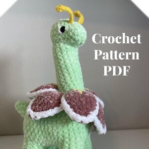 May include: Crochet pattern PDF for a green and brown amigurumi toy that resembles a flower with a long neck. The toy has a yellow antenna and black eyes.