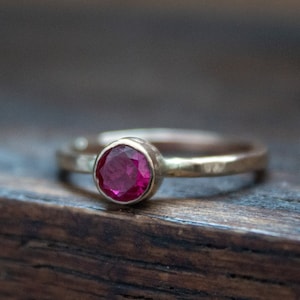 May include: A simple gold band ring with a single, round, faceted, pink gemstone.
