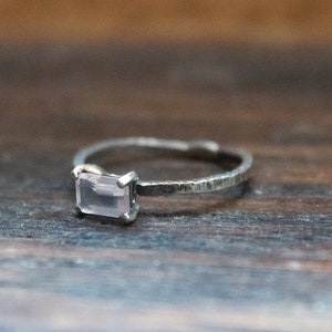May include: A silver ring with a light pink rectangular gemstone. The ring has a textured band.