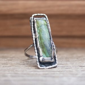 May include: A silver ring with a green and blue gemstone set in a textured silver frame.