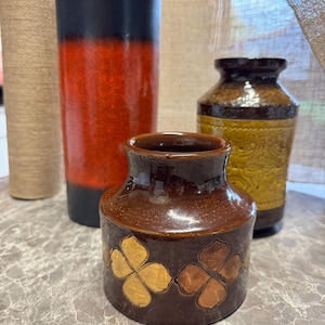 May include: Three ceramic vases in different sizes and colours. The largest vase is black and orange, the medium vase is brown with gold and copper accents, and the smallest vase is brown with gold accents.