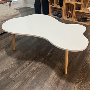 May include: White coffee table with an organic, free-form shape and a light wood base. The table is sitting on a dark wood floor.