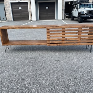 May include: A wooden media console with a slatted design on one side and a shelf on the other. The console is supported by hairpin legs and has a dark brown stain.