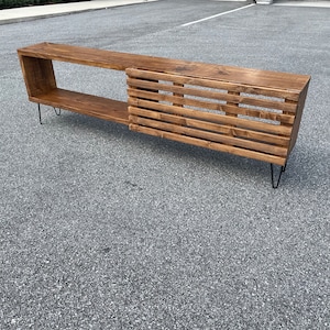 May include: A long, wooden media console with a slatted design on the right side and a shelf on the left. The console is supported by hairpin legs.