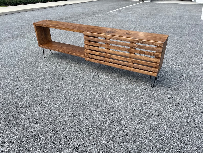 May include: A long, wooden media console with a slatted design on the right side and a shelf on the left. The console is supported by hairpin legs.