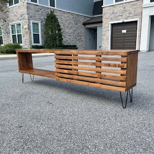 May include: A wooden media console with a slatted design and a shelf. The console is supported by black hairpin legs.
