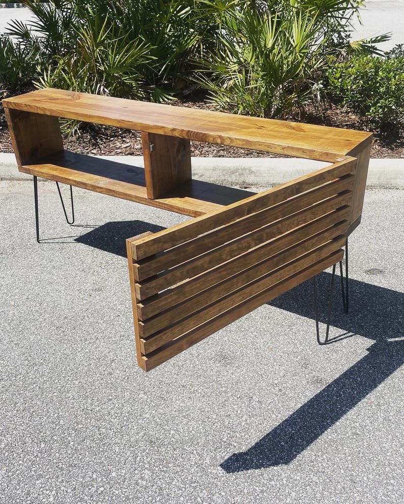 May include: A wooden entertainment center with a unique angled design. The unit features a shelf, two compartments, and a slatted back panel. It is supported by hairpin legs.