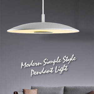 May include: A white modern simple style pendant light hanging over a gray sofa with a brown throw pillow. The light has a circular, flat design.