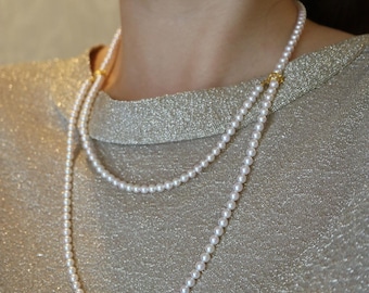 May include: A double-strand pearl necklace with gold clasps. The necklace is composed of small, round, white pearls. The background is a gold-colored, textured fabric. A matching pearl earring is visible.