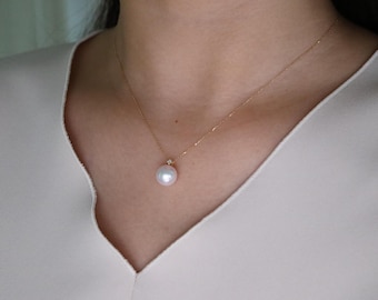 Puede incluir: Delicado collar de oro con un colgante de perla grande y redondo. La perla es blanca con un brillo iridiscente sutil. Un pequeño acento brillante se encuentra encima de la perla. Es una fina pieza de joyería.