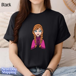 A person wearing a black t-shirt with a cartoon illustration of a young girl with braided hair and blue eyes.