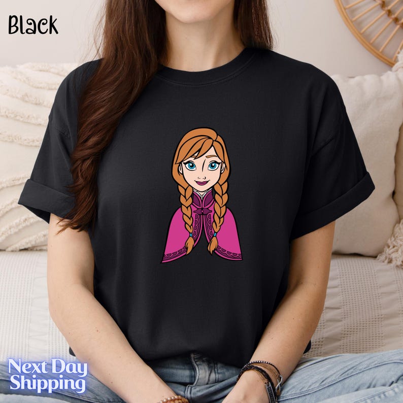 A person wearing a black t-shirt with a cartoon illustration of a young girl with braided hair and blue eyes.