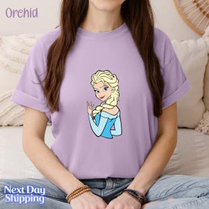A woman wearing a purple t-shirt with a cartoon image of a blonde woman with blue eyes and blonde braids.