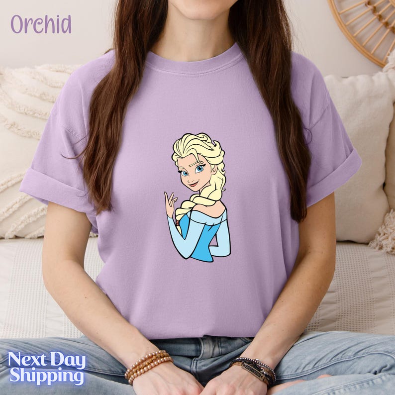 A woman wearing a purple t-shirt with a cartoon image of a blonde woman with blue eyes and blonde braids.