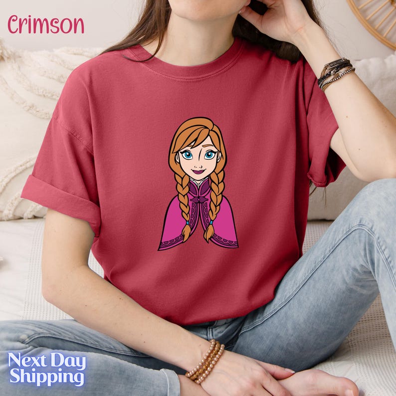 A woman wearing a red t-shirt with a cartoon illustration of a young girl with braided hair.