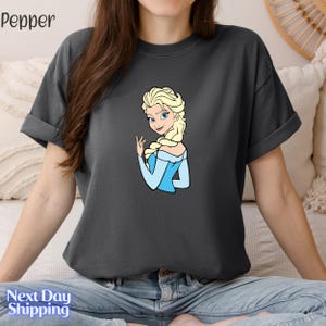 A woman wearing a gray t-shirt with a graphic of a blonde woman in blue dress.