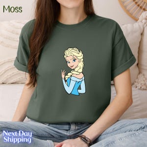 A woman wearing a green t-shirt with a cartoon image of a blonde woman.