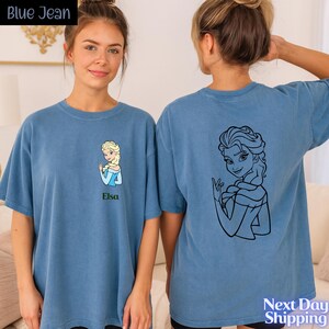 A young woman wearing a blue t-shirt with a cartoon character printed on it, standing next to another woman.