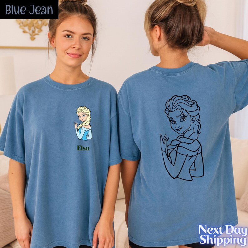 A young woman wearing a blue t-shirt with a cartoon character printed on it, standing next to another woman.