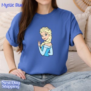 A woman wearing a blue t-shirt with a cartoon image of a blonde woman.
